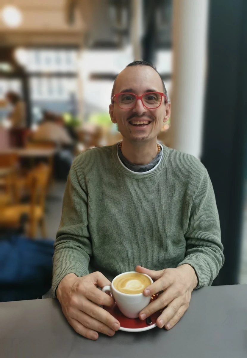 Erwin Strobl mit roter Brille im Caf&eacute;, eine Tasse Kaffee in den H&auml;nden